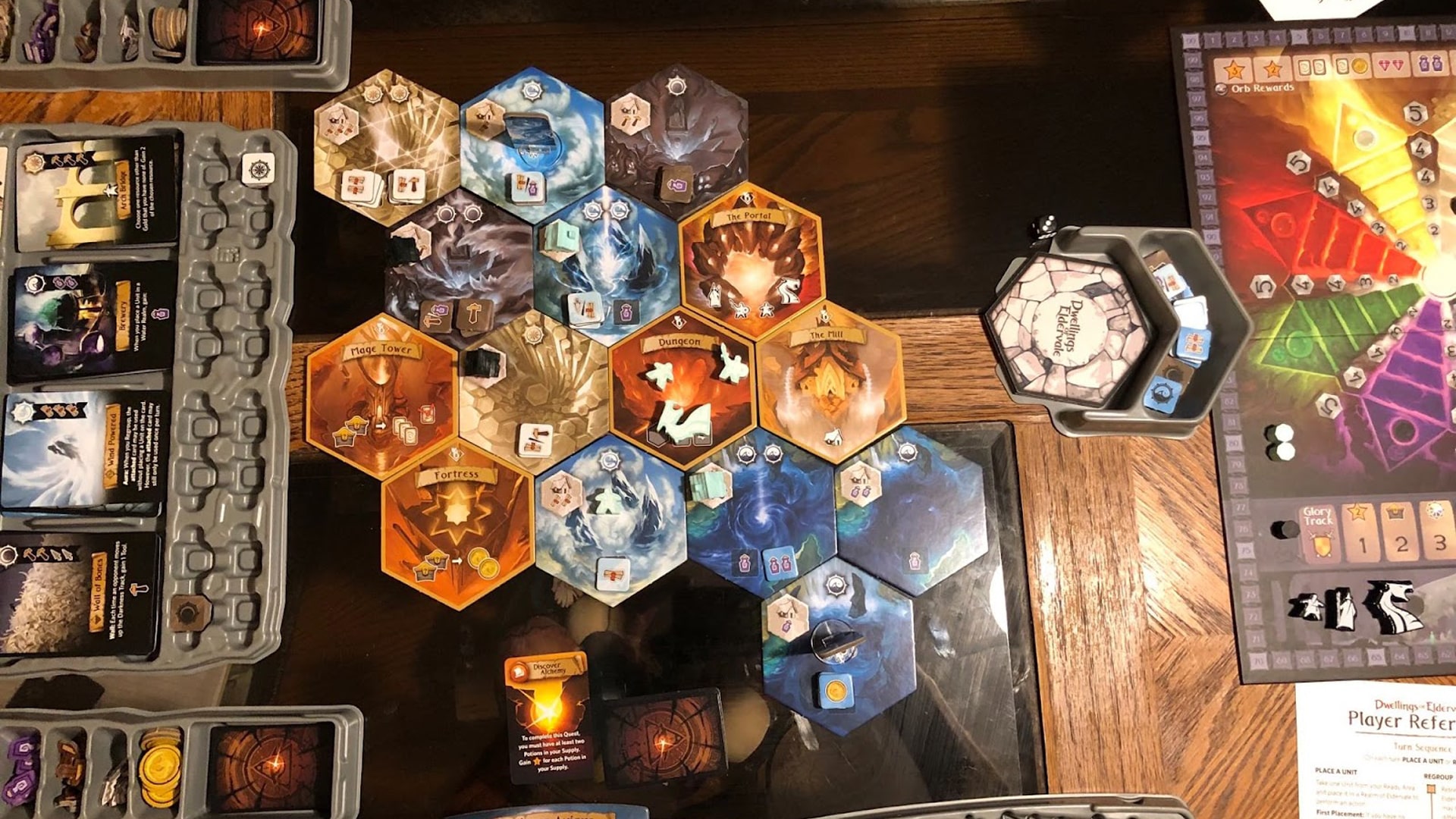 Gameplay layout of Dwellings of Eldervale, featuring colorful boards, cards, and fantasy-themed miniatures, highlighting the game's immersive world-building.